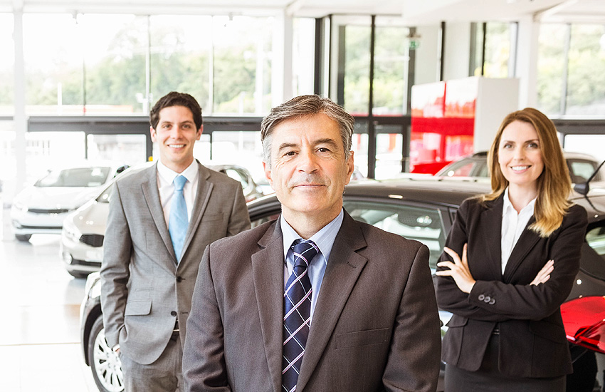 Car dealership team standing in a showroom with vehicles in the background.