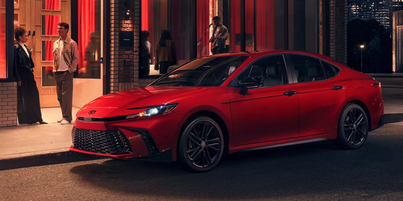 Red Toyota Camry parked on a city street at night in front of a building with glowing red windows